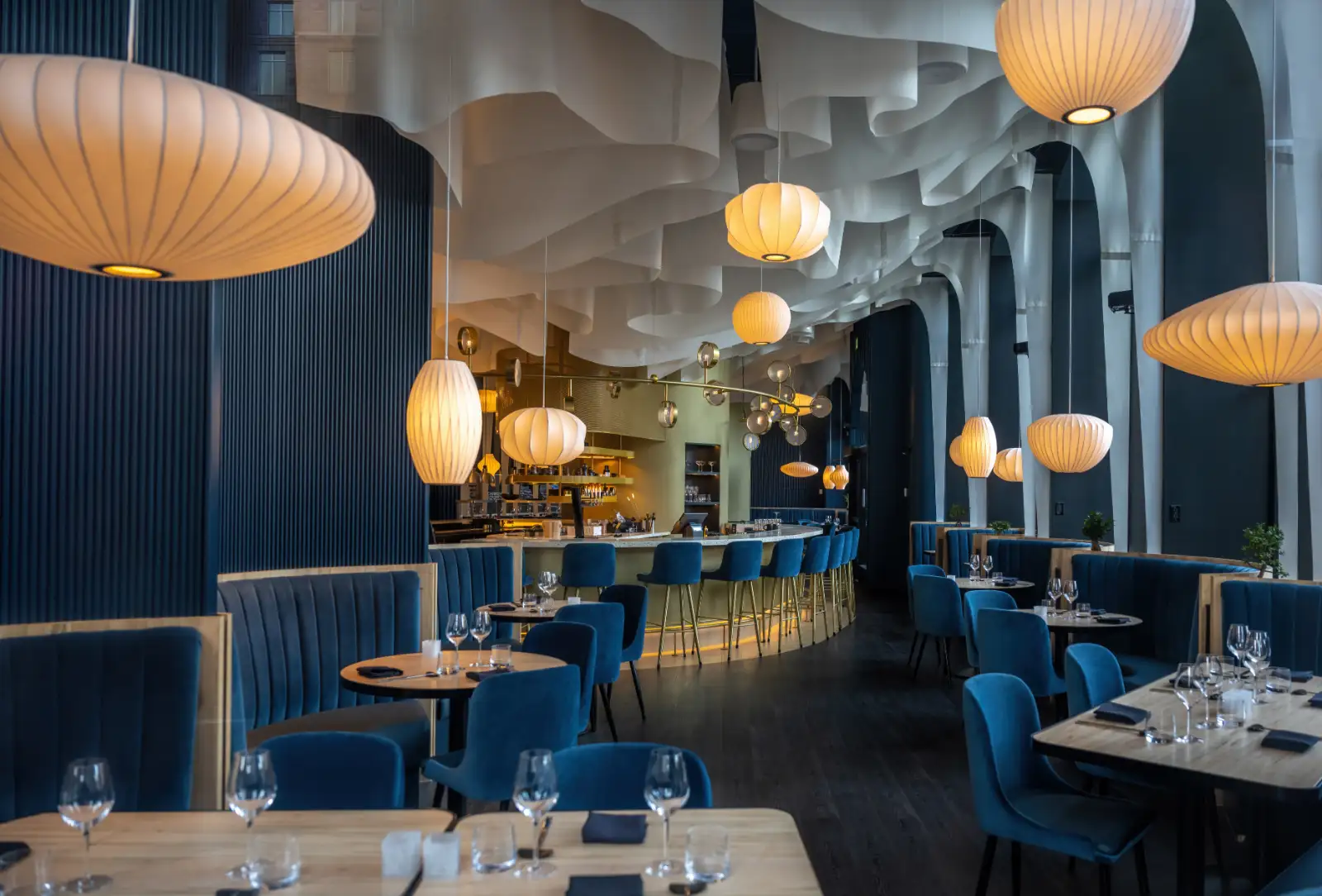 A dining room with blue velvet booths, set tables and paper lantern lights