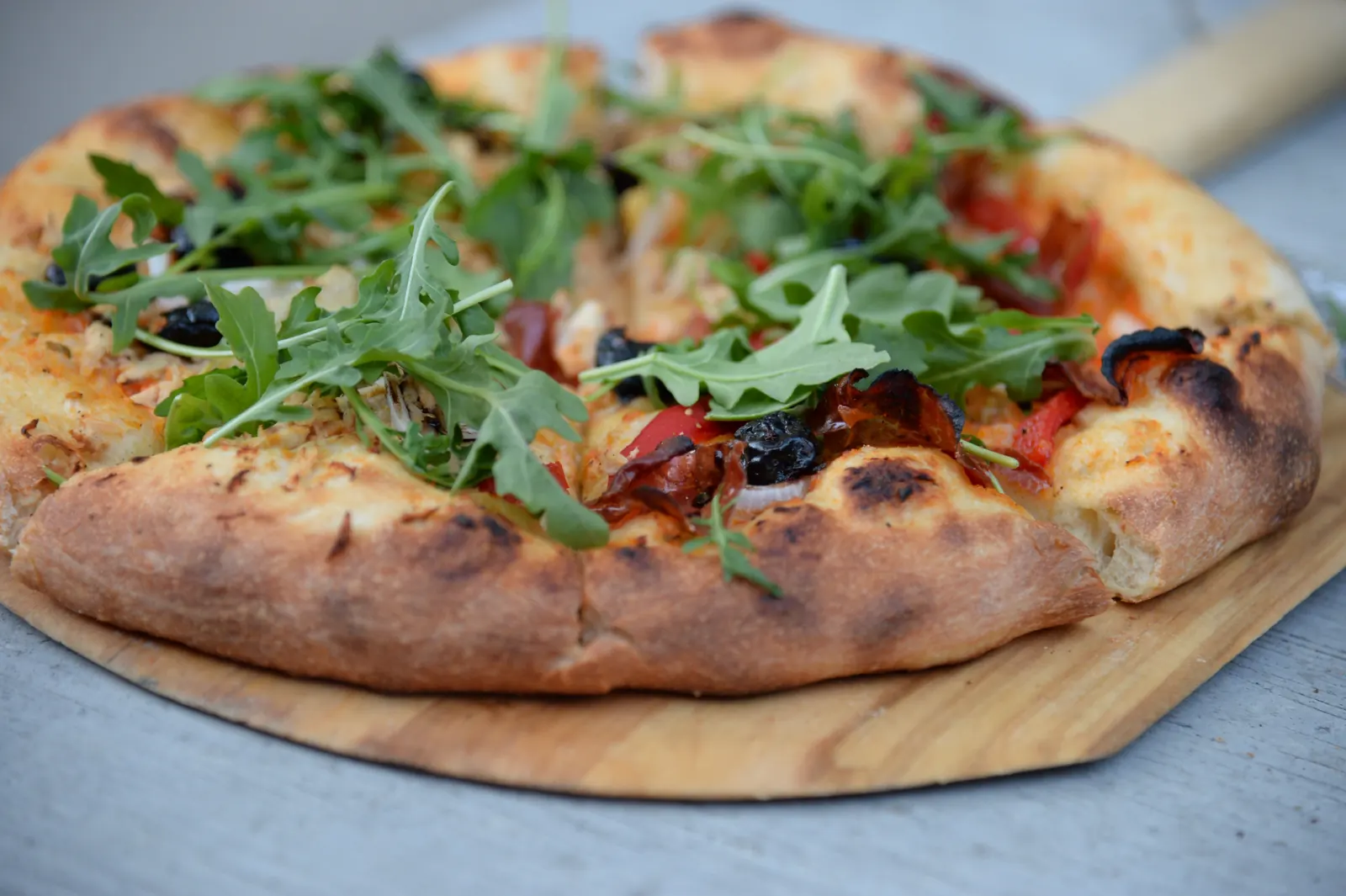 A pizza with arugula and olives on a wooden peel